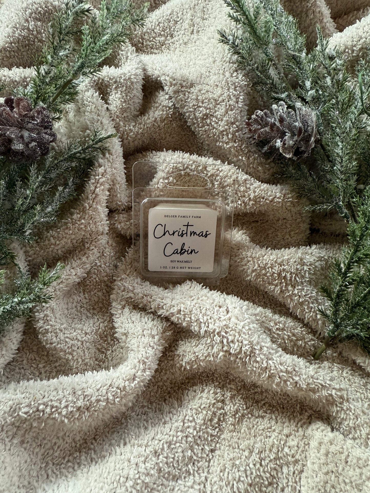 Candle labeled 'Christmas Cabin' on a textured beige surface with greenery