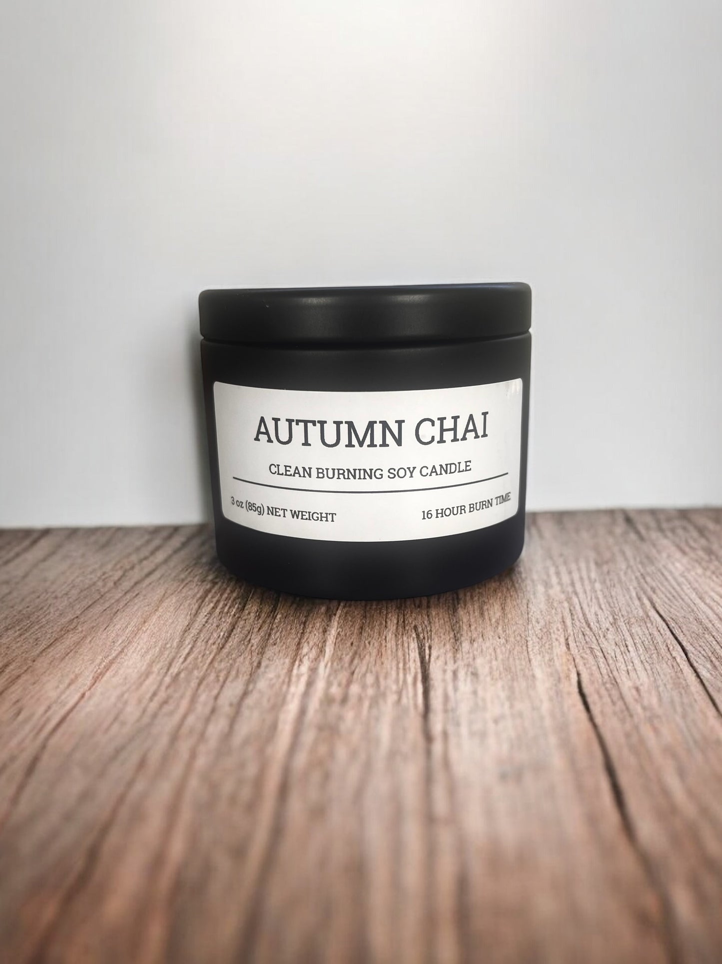 Candle labeled 'Autumn Chai' on a wooden surface with a white background