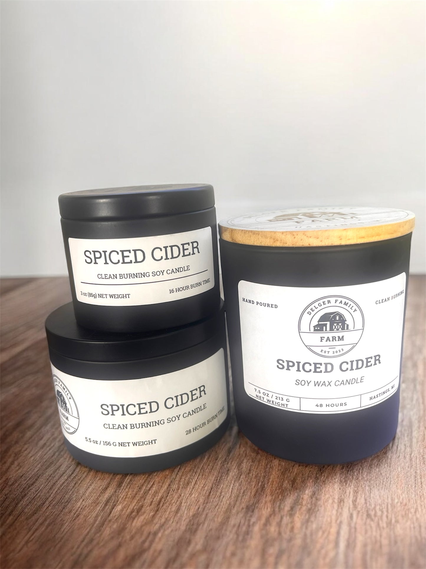 Three 'Spiced Cider' candles stacked on a wooden surface with a neutral background.