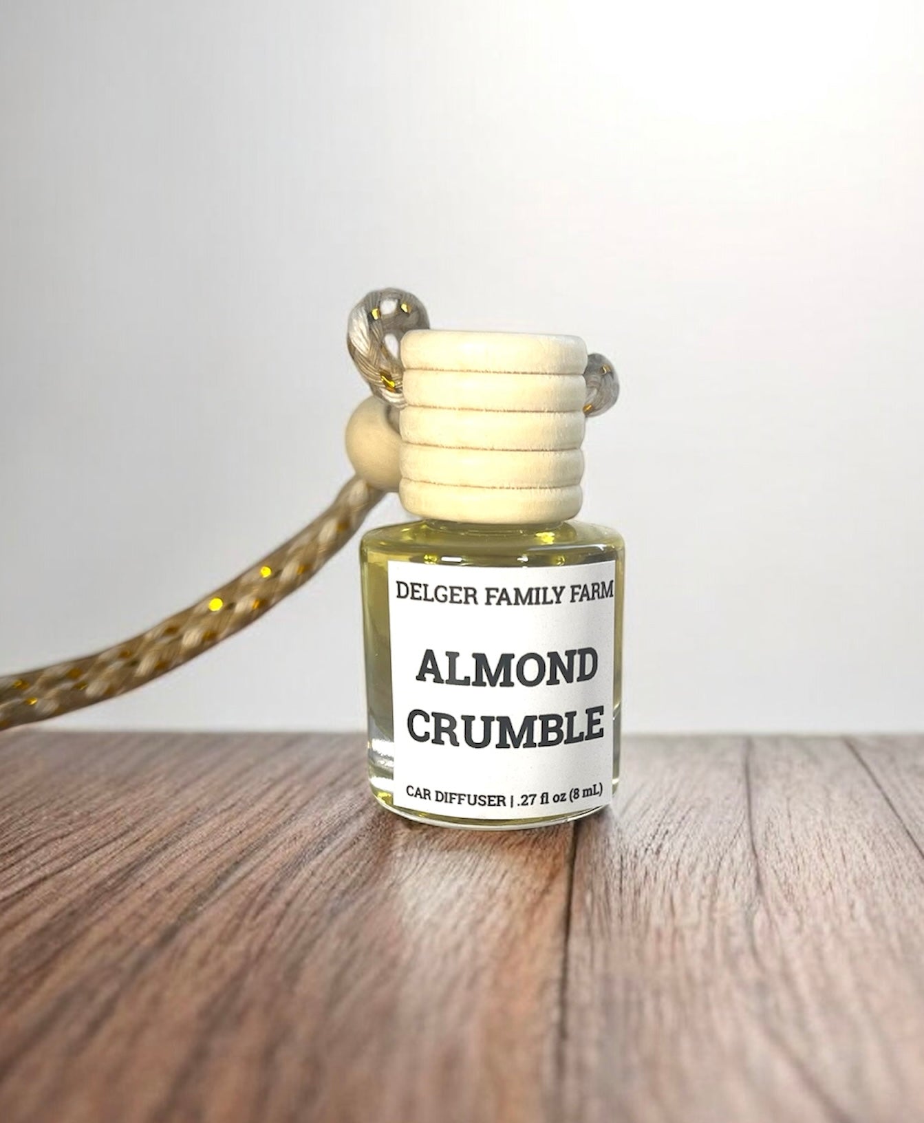 Bottle of Delger Family Farms Almond Crumble car diffuser on a wooden surface with a white background