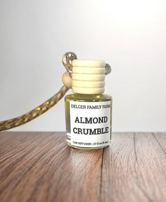 Bottle of Delger Family Farms Almond Crumble car diffuser on a wooden surface with a white background