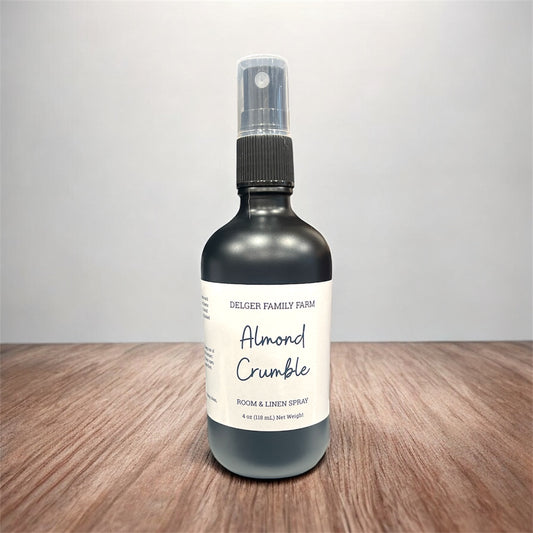 Bottle of almond crumble room and linen spray on a wooden surface with a gray background