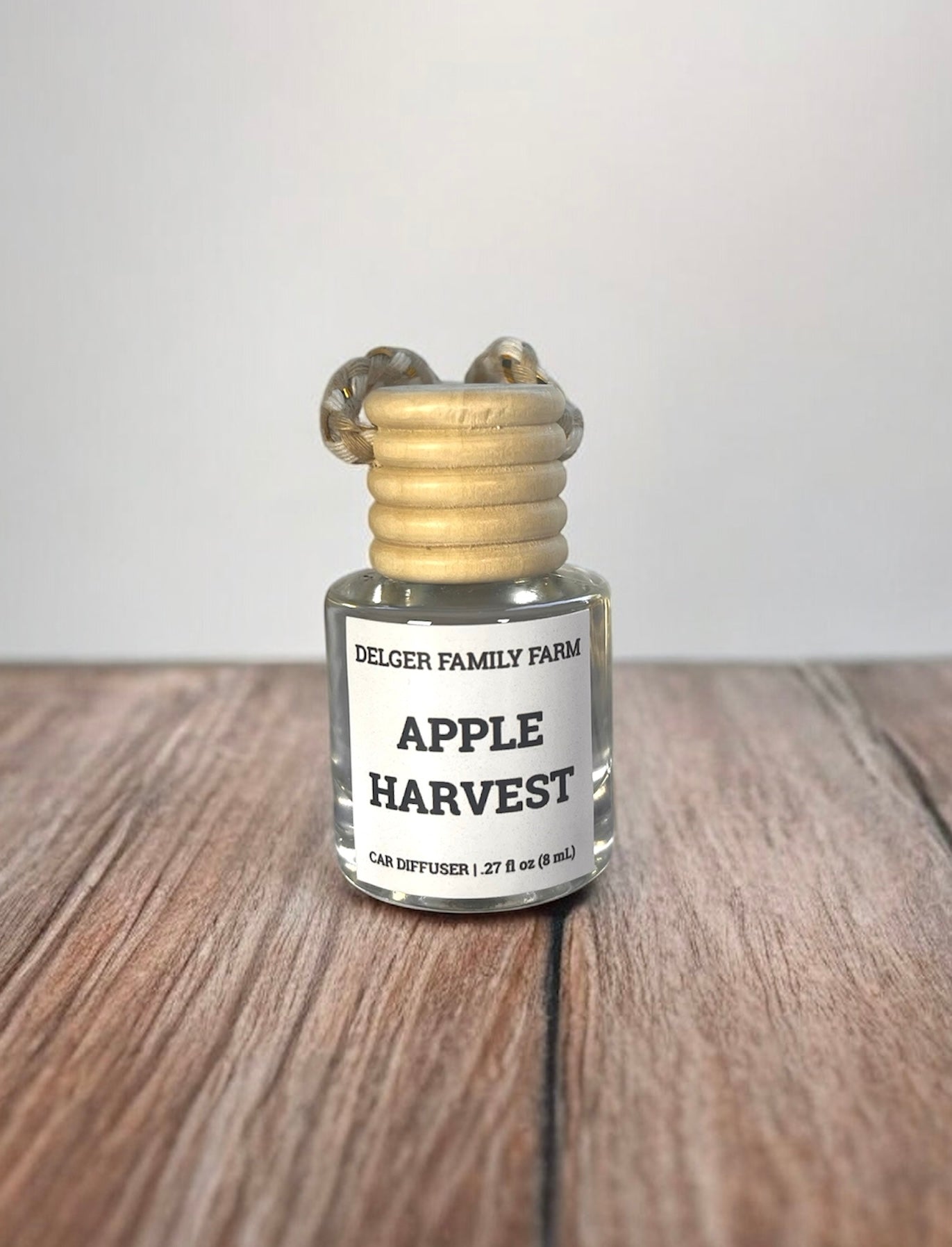 Small glass bottle labeled 'Apple Harvest' by Delger Family Farm on a wooden surface with a white background.