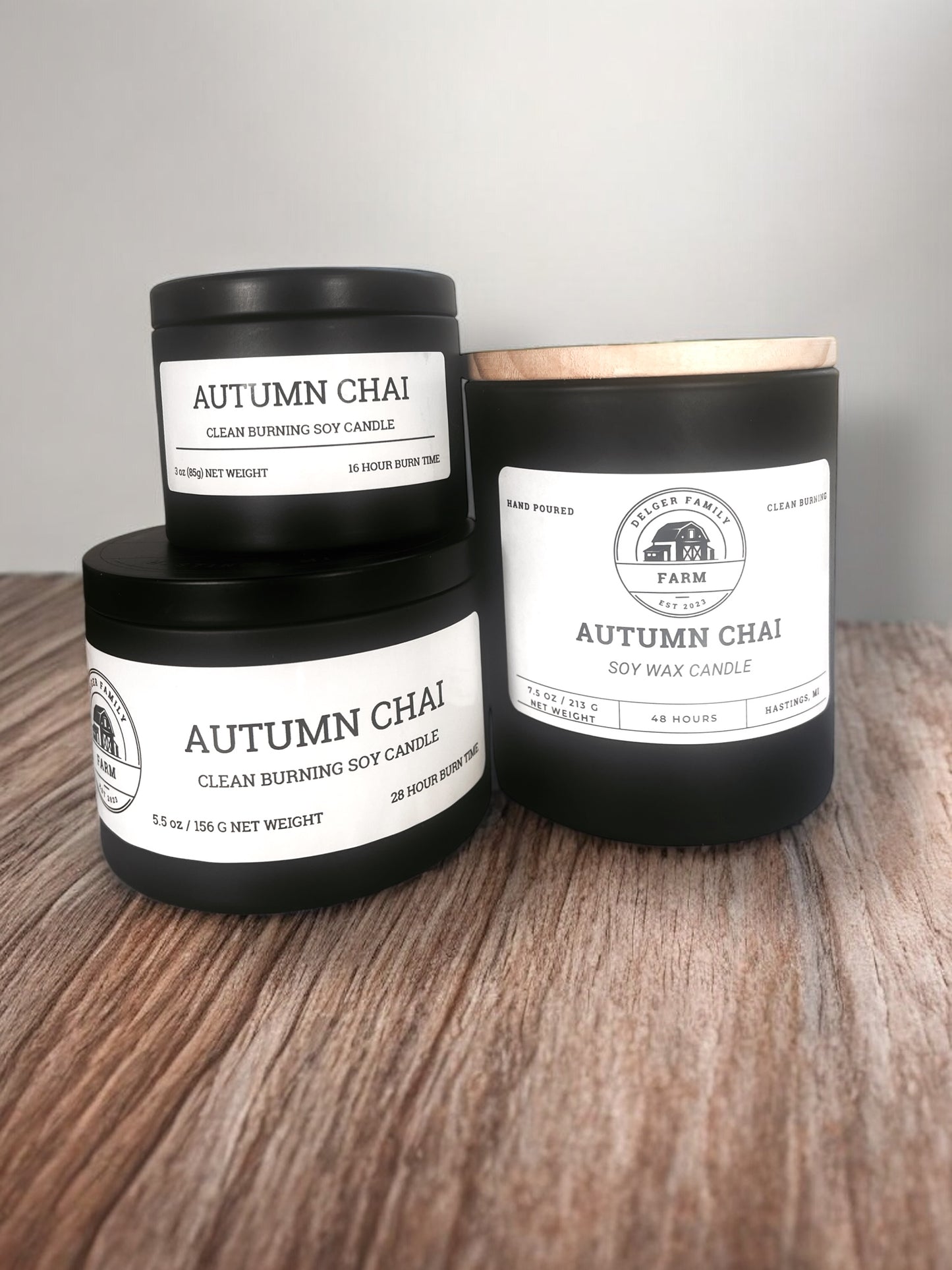 Three 'Autumn Chai' candles from Walker Family Farm on a wooden surface with a gray background.