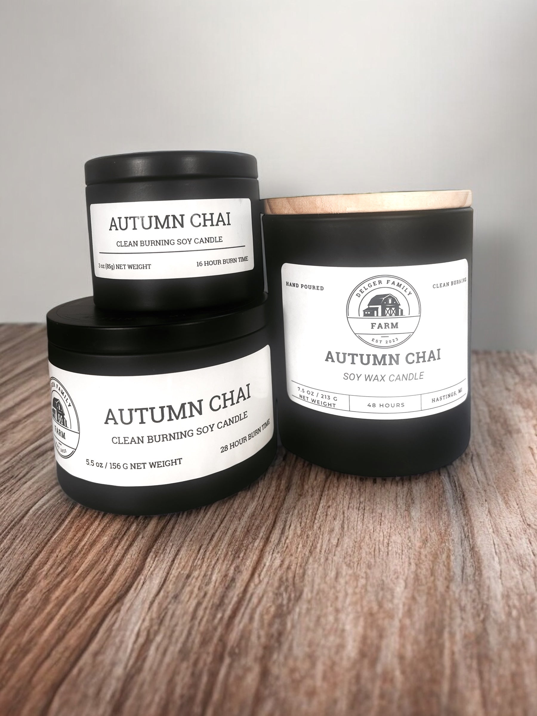 Three 'Autumn Chai' candles from Walker Family Farm on a wooden surface with a gray background.