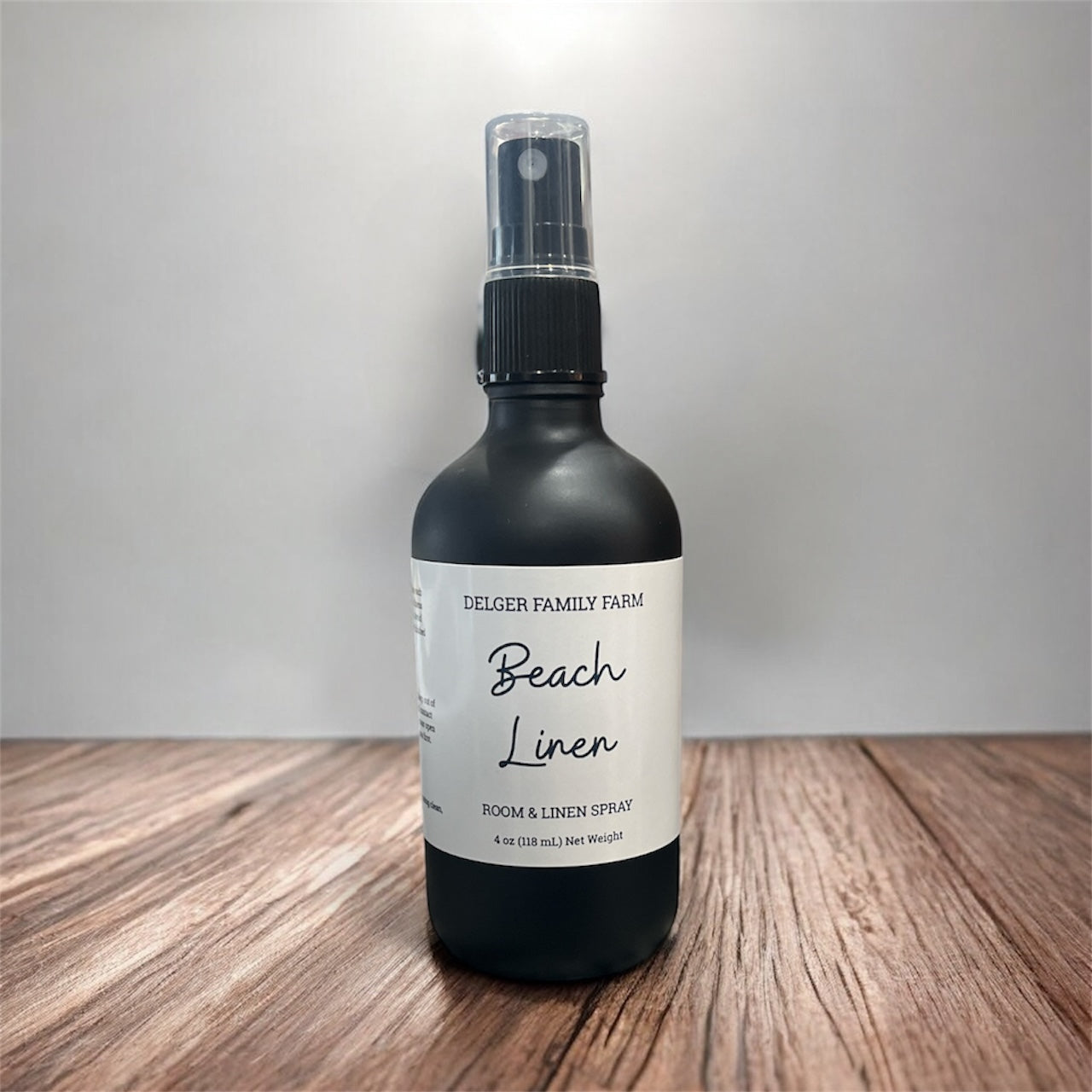 Black spray bottle labeled 'Beach Linen' on a wooden surface with a neutral background