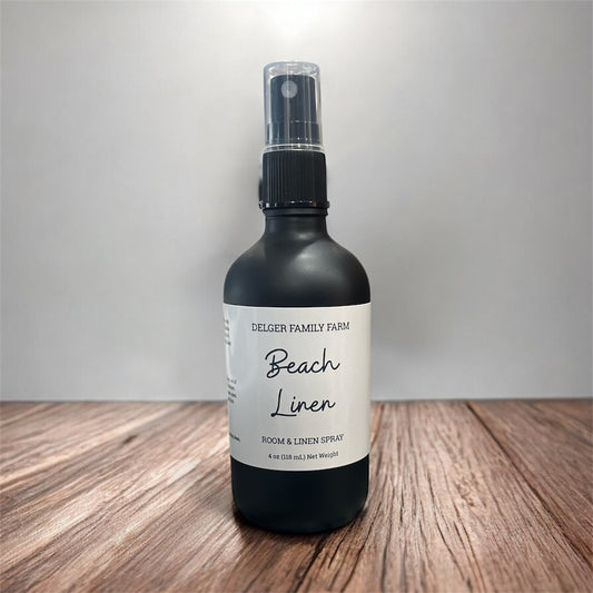 Black spray bottle labeled 'Beach Linen' on a wooden surface with a neutral background