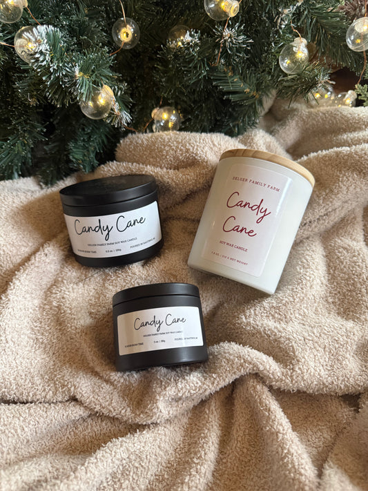 Three 'Candy Cane' candles on a textured surface with a Christmas tree in the background