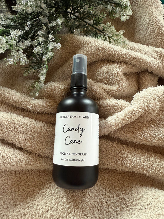 Bottle of 'Candy Cane' room & linen spray on a textured surface with flowers in the background
