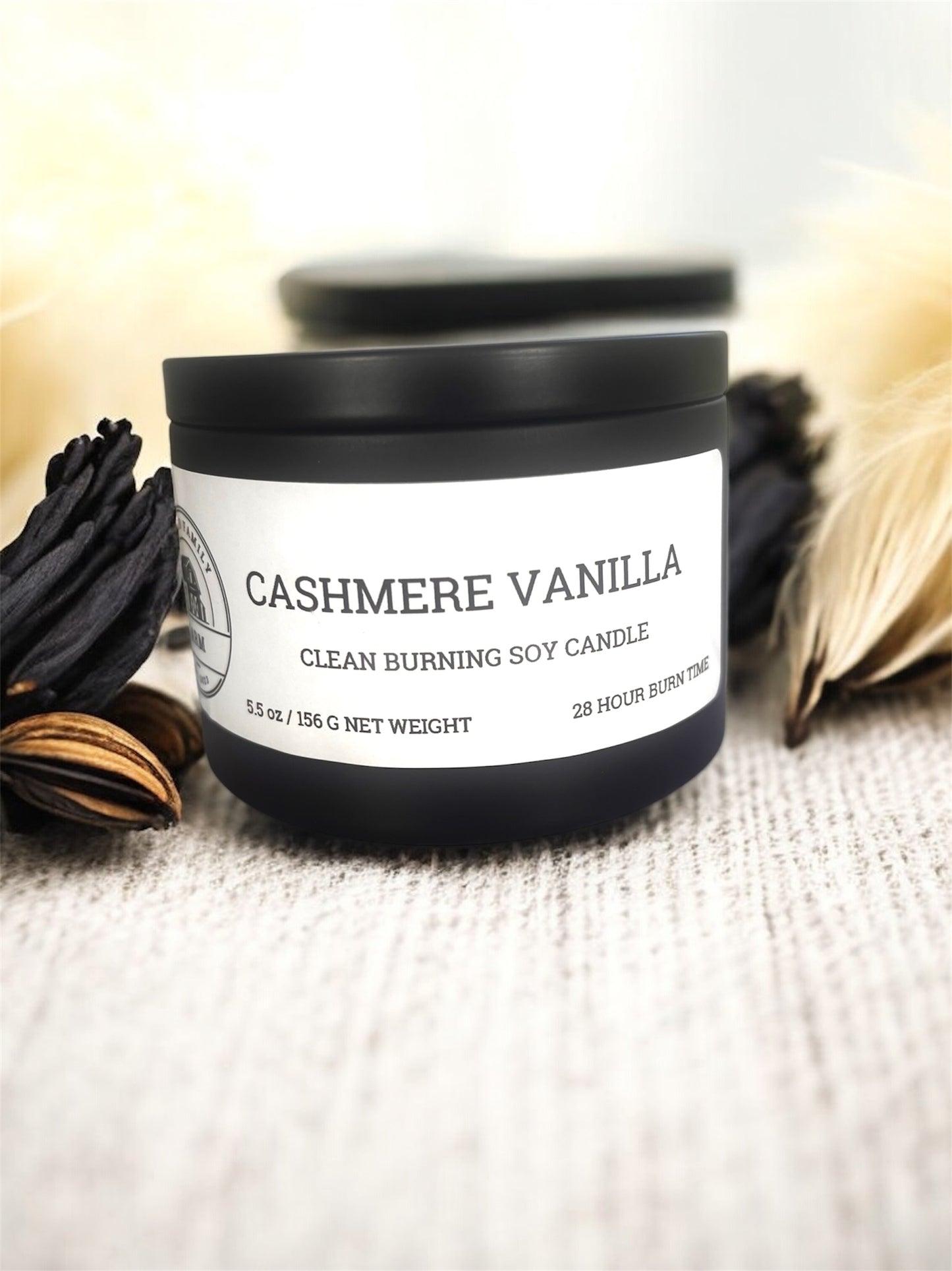 Black candle tin labeled cashmere vanilla sitting on cream fabric