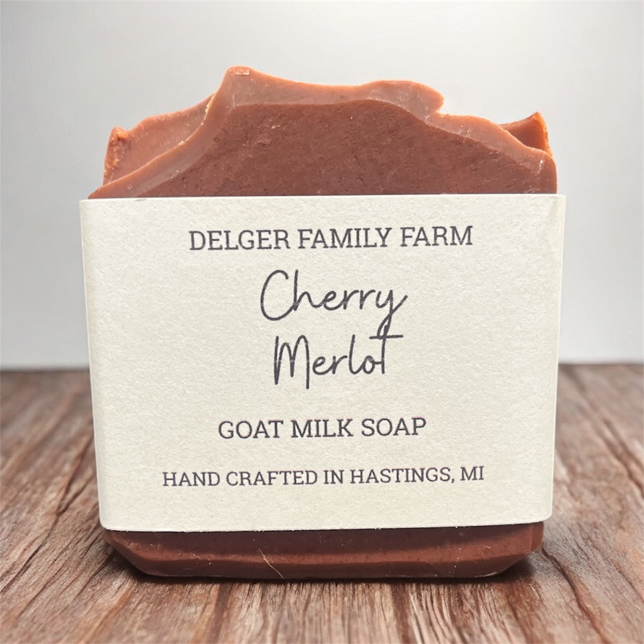 Bar of cherry merlot goat milk soap from Delger Family Farm on a wooden surface with a gray background.