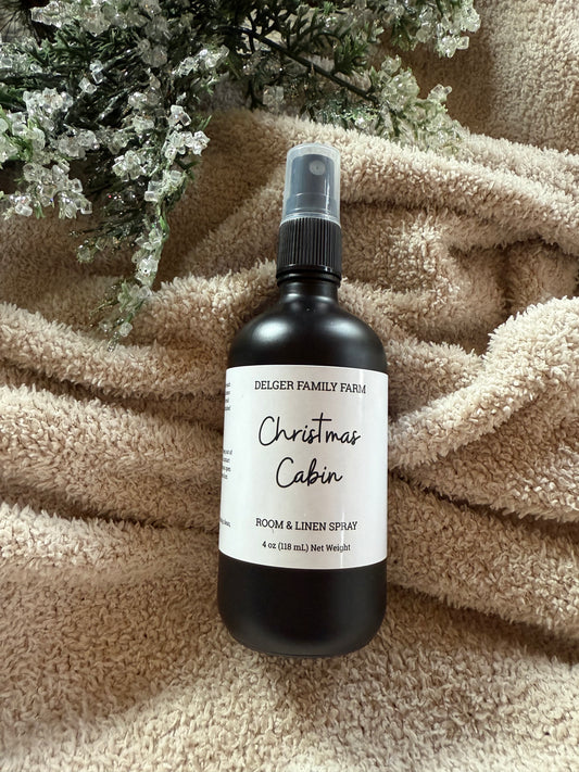 Black spray bottle labeled 'Christmas Cabin' on a textured surface with decorative elements.