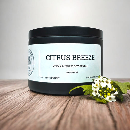 Candle labeled 'Citrus Breeze' on a wooden surface with flowers.