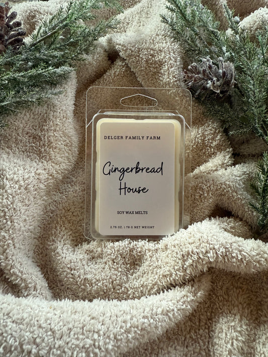 Packaged gingerbread house soy wax melt on a textured surface with greenery