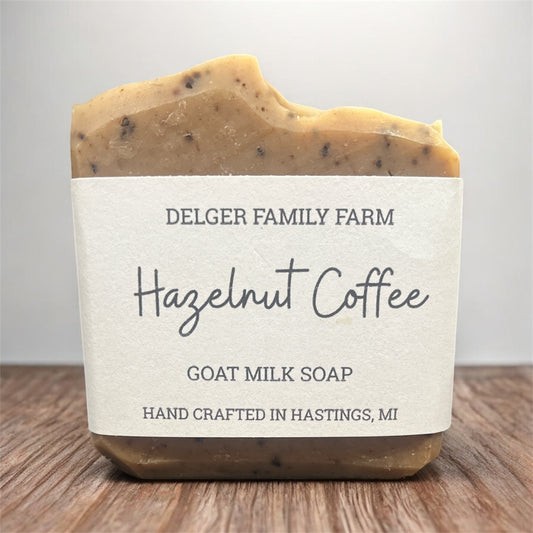 Bar of goat milk soap labeled 'Hazelnut Coffee' from Delger Family Farm on a wooden surface.