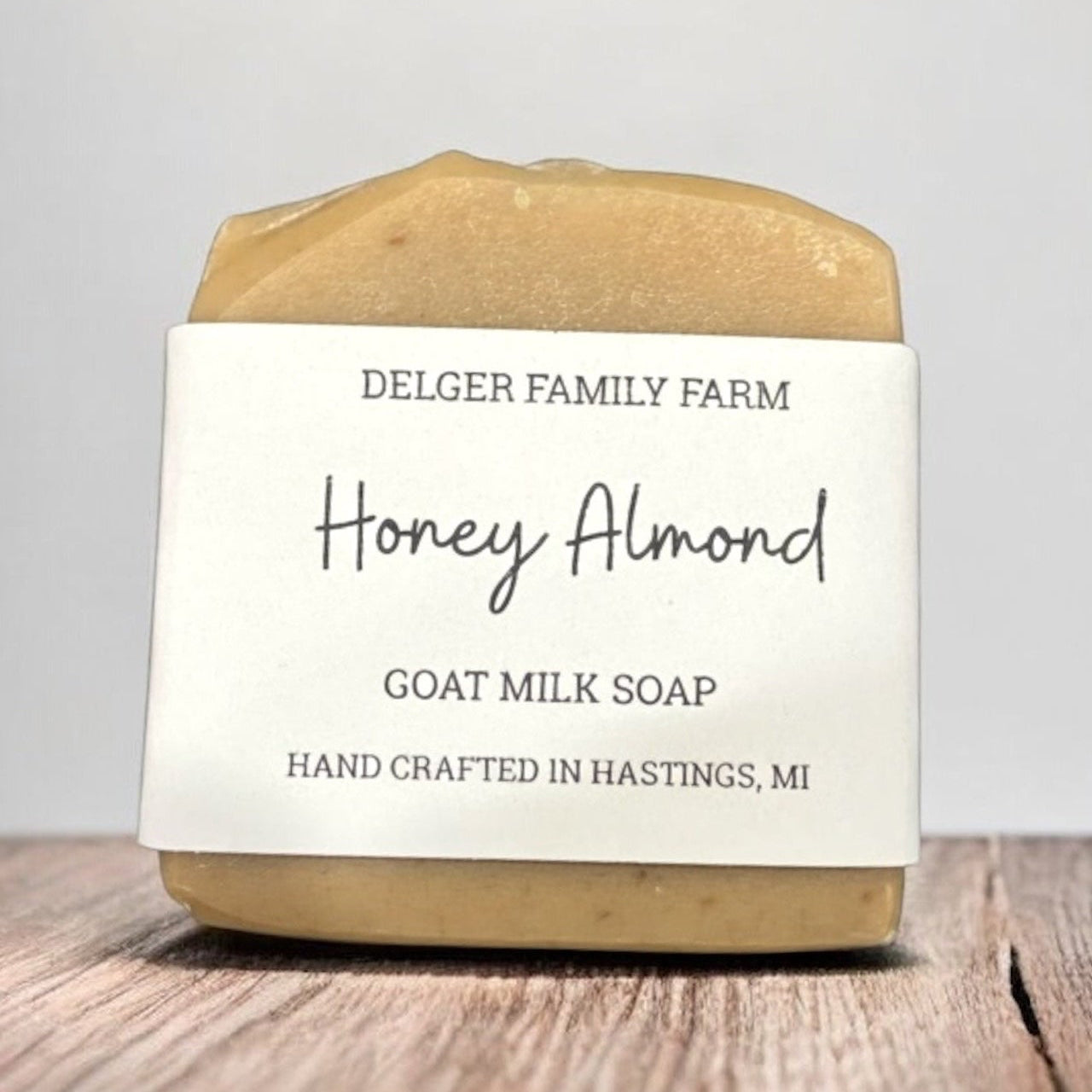 Bar of honey almond goat milk soap from Delger Family Farm on a wooden surface with a gray background