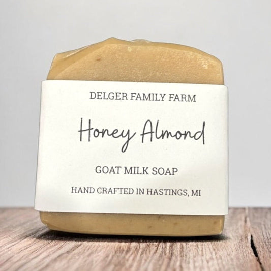 Bar of honey almond goat milk soap from Delger Family Farm on a wooden surface with a gray background