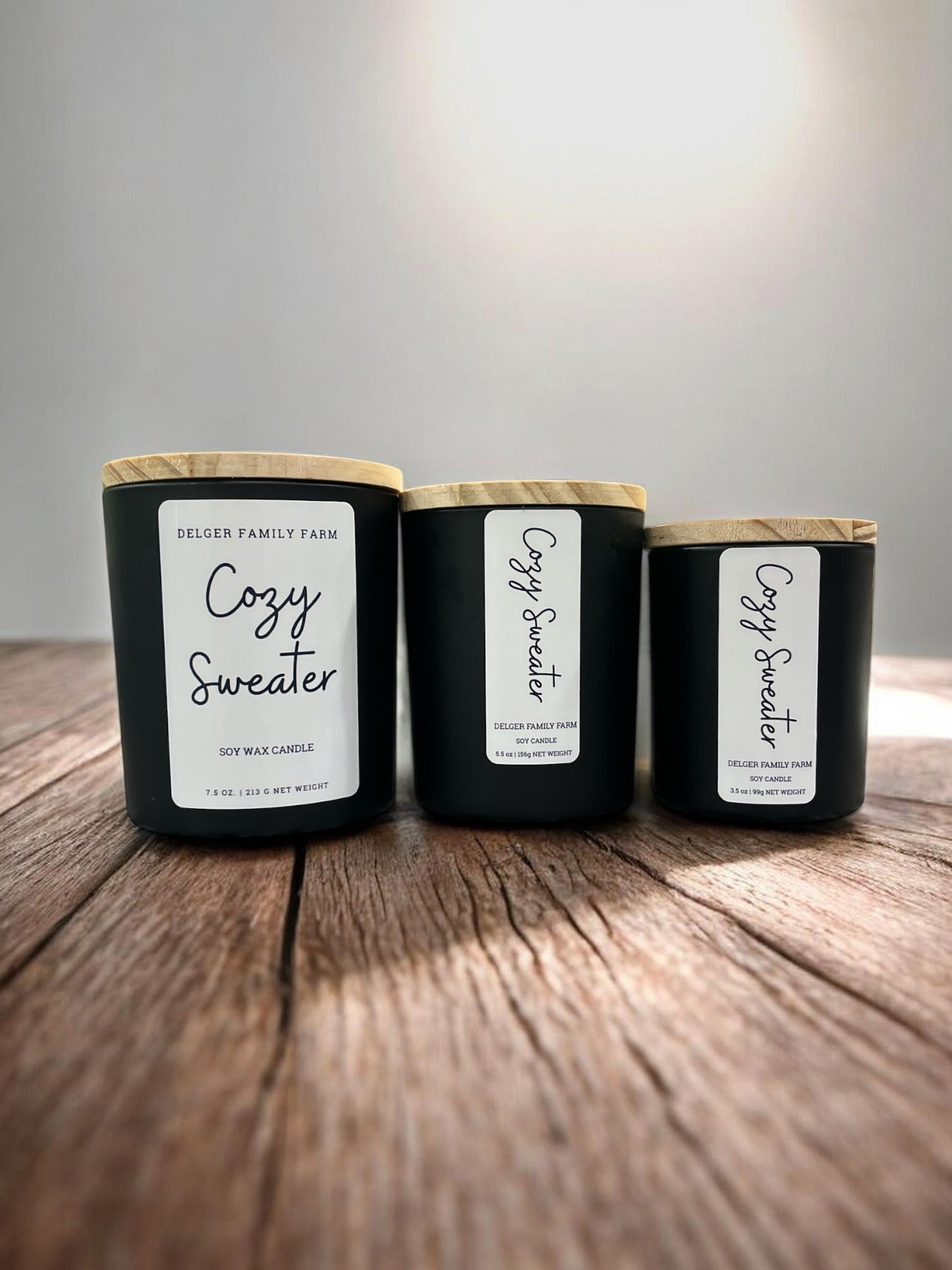 3 sizes of candles in black jars on wooden table with gray background 