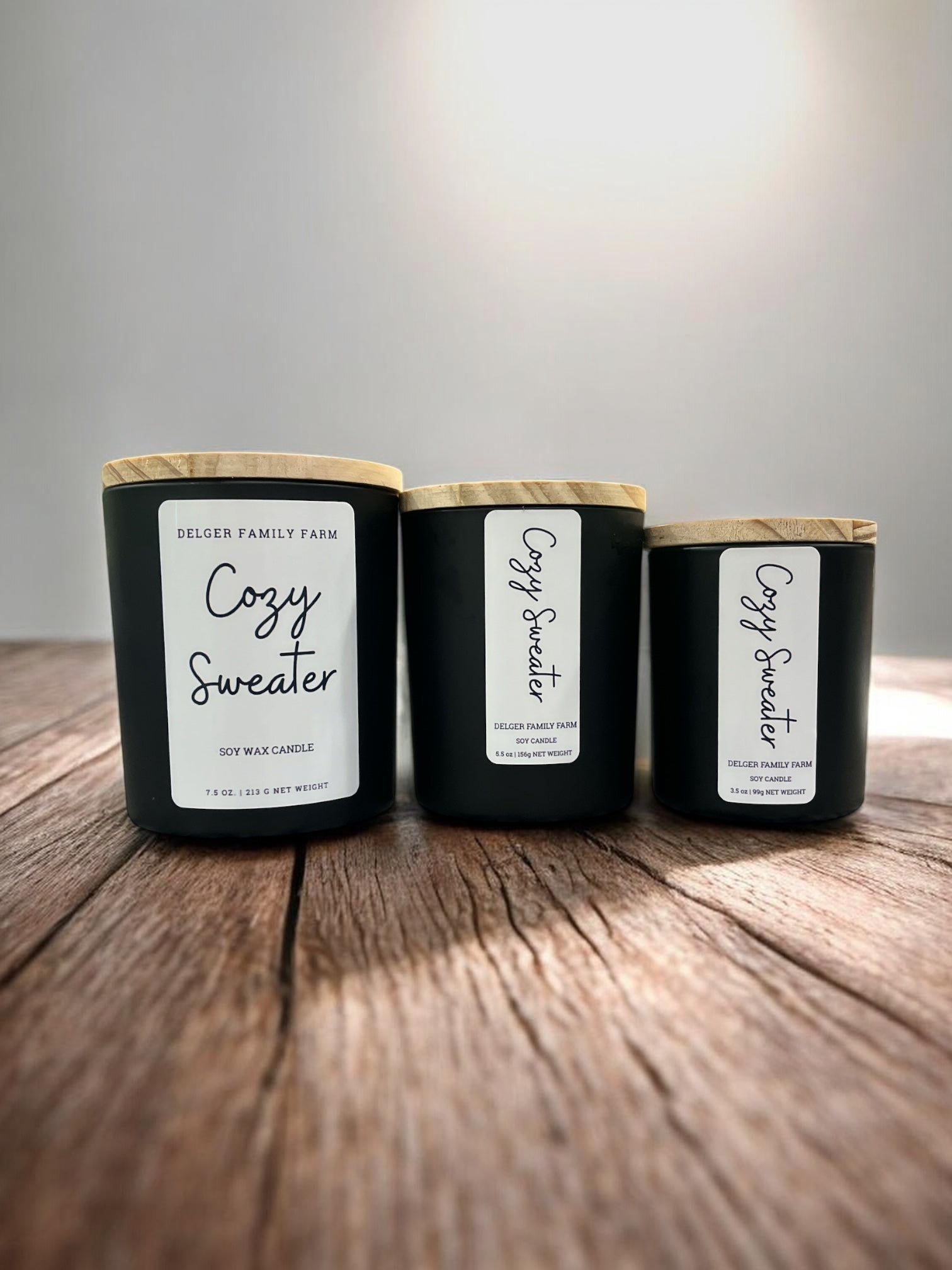3 sizes of candles in black jars on wooden table with gray background 