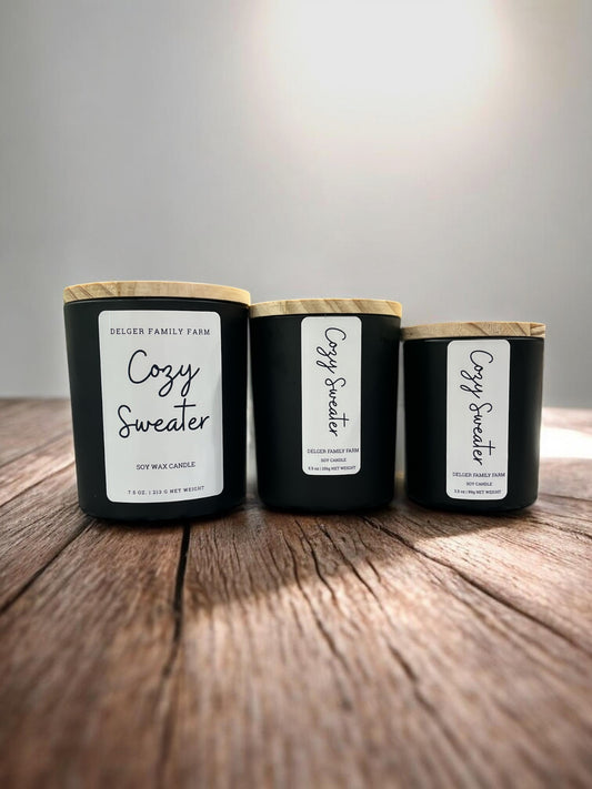 3 sizes of candles in black jars on wooden table with gray background 