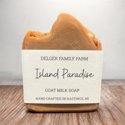Bar of goat milk soap labeled 'Island Paradise' from Delger Family Farm on a wooden surface.