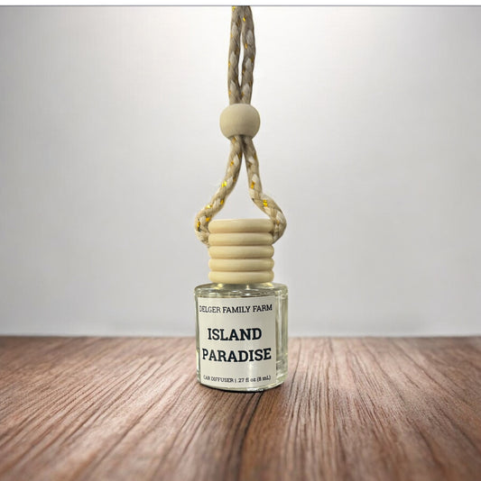 Car air freshener labeled 'Island Paradise' by Delger Family Farm on a wooden surface with a white background.