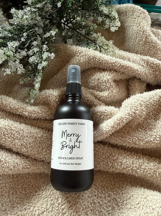Room & Linen Spray bottle labeled 'Merry & Bright' on a textured surface with floral decor.