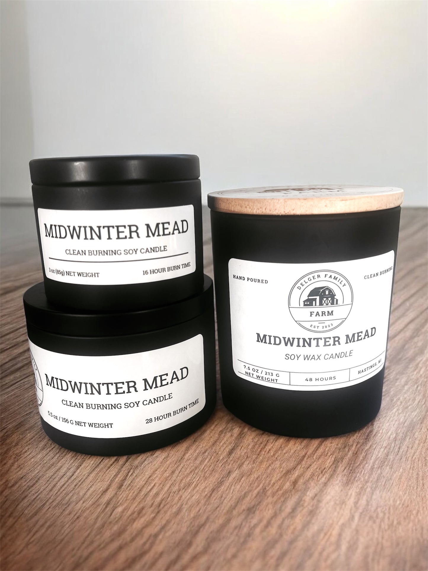 Three 'Midwinter Mead' candles on a wooden surface with a neutral background