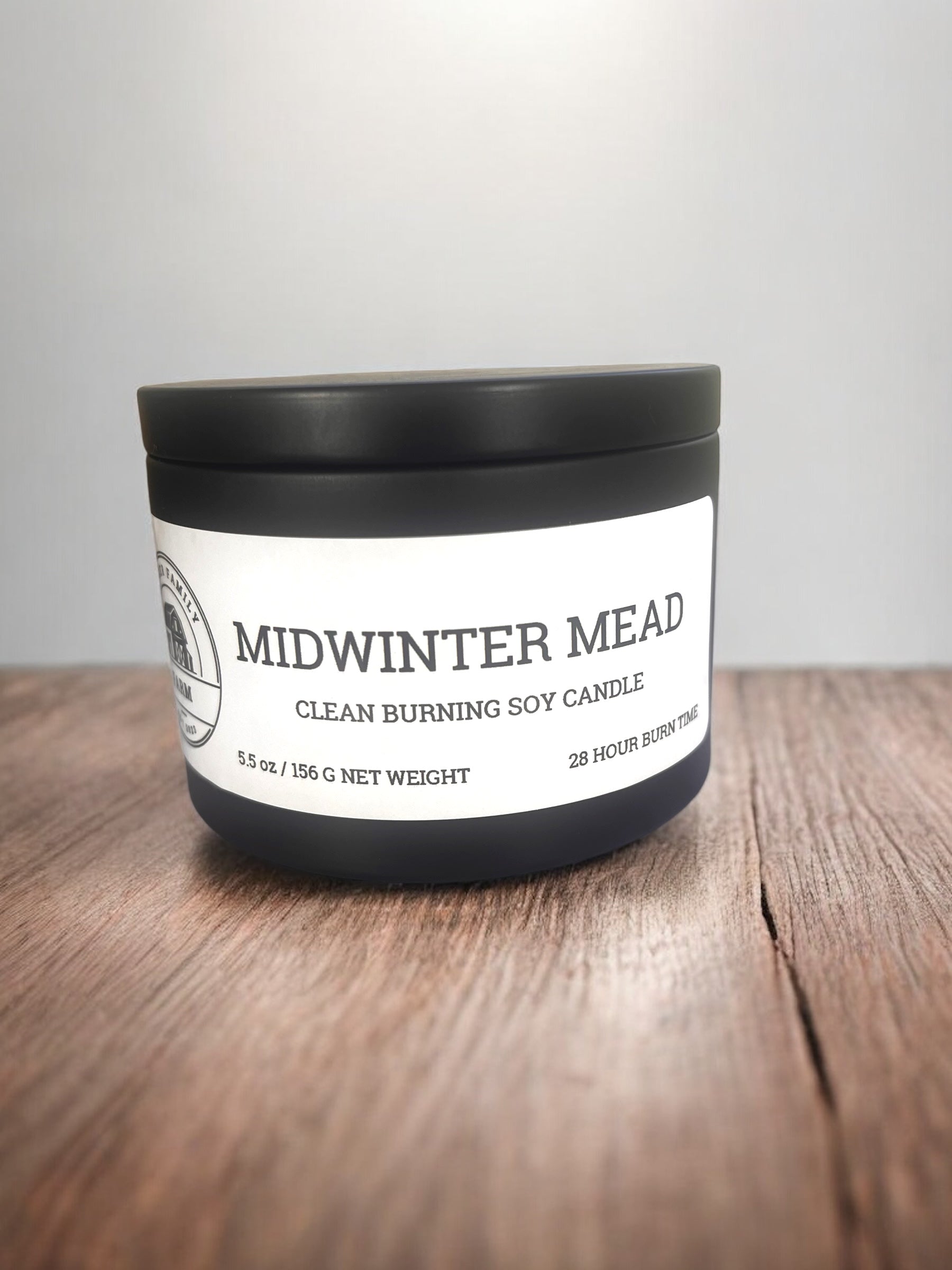 Candle labeled 'Midwinter Mead' on a wooden surface with a light gray background