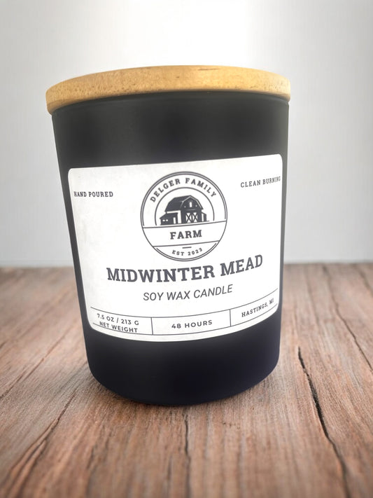 Black candle with a wooden lid on a wooden surface, featuring a label with text and branding.