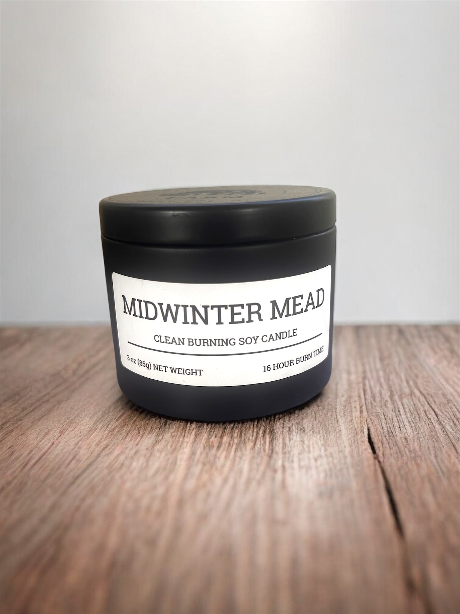 Candle labeled 'Midwinter Mead' on a wooden surface with a white background