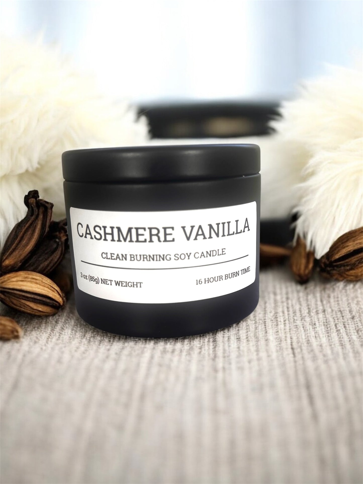 Black candle tin labeled cashmere vanilla resting on fabric 