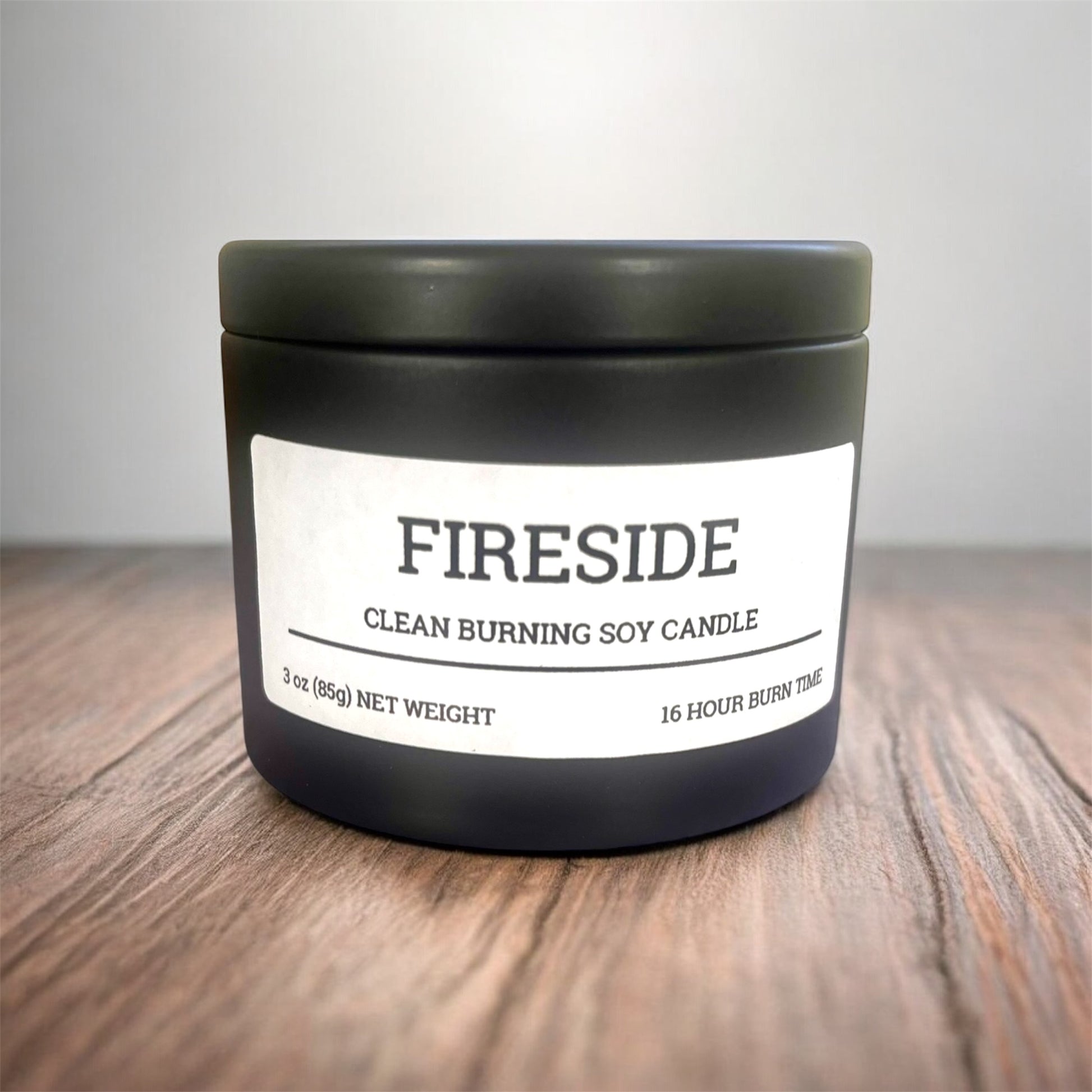 Black candle jar labeled 'Fireside' on a wooden surface with a neutral background
