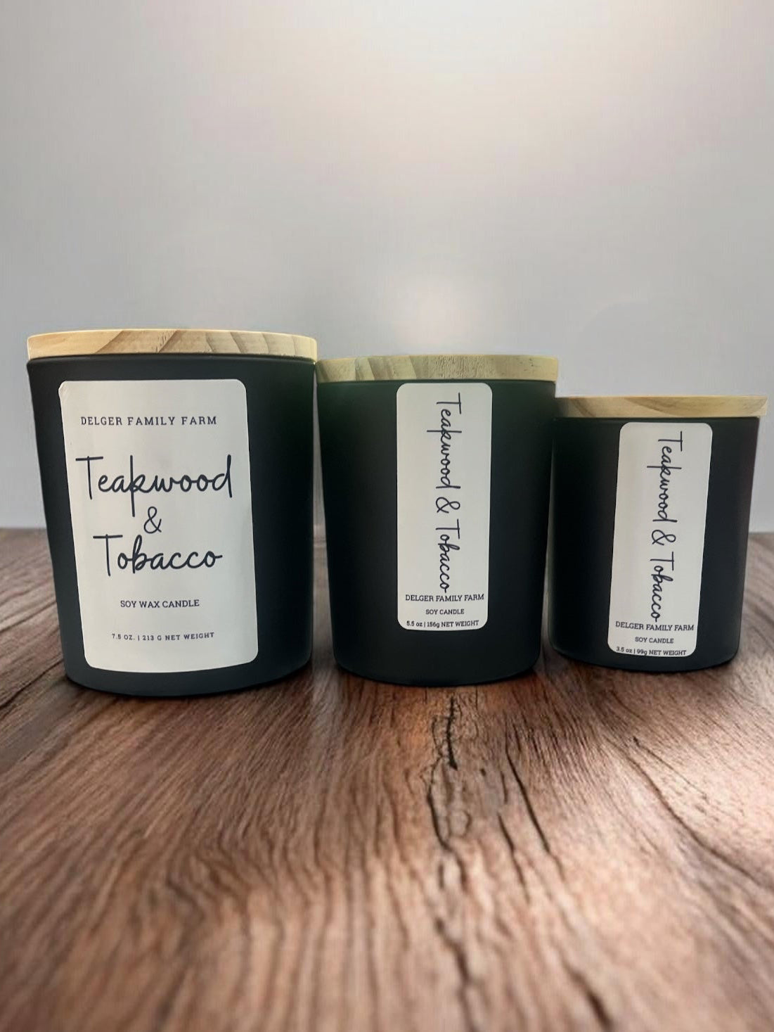 Three candles labeled 'Teakwood & Tobacco' on a wooden surface with a neutral background