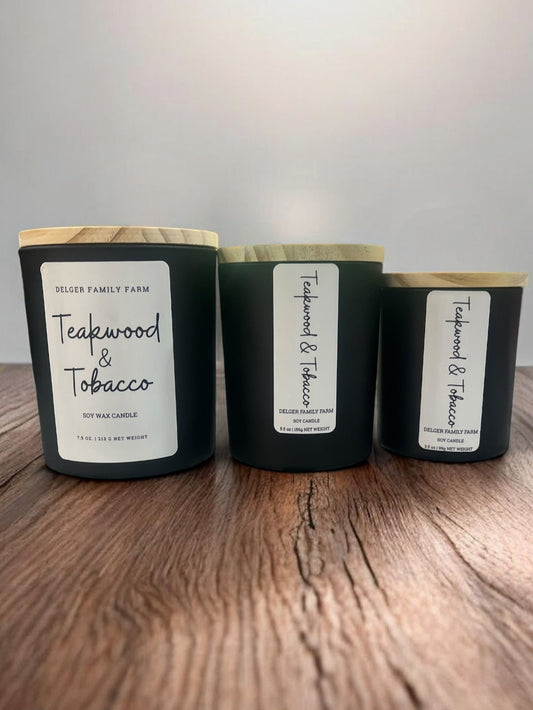 Three candles labeled 'Teakwood & Tobacco' on a wooden surface with a neutral background
