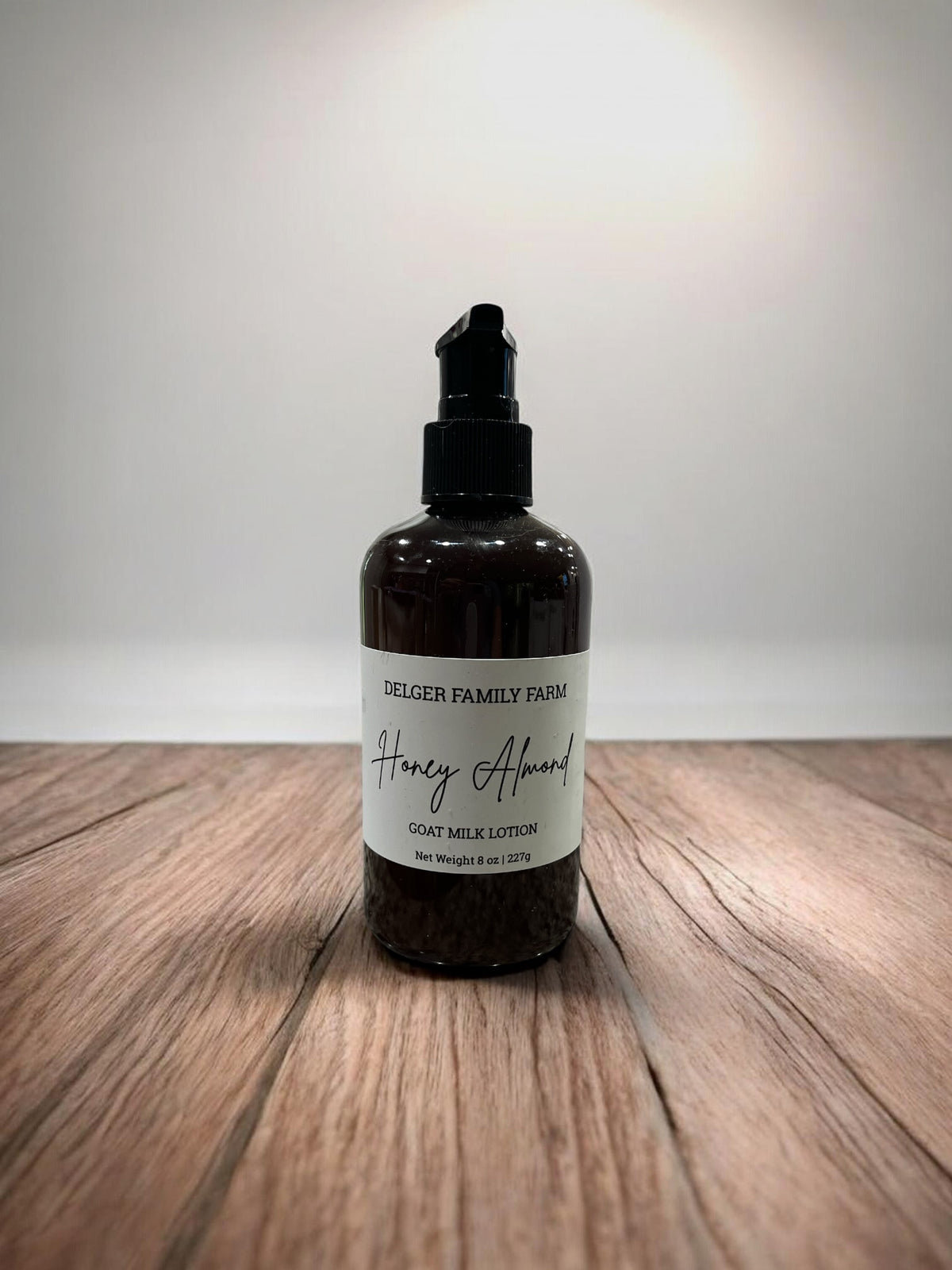 Bottle of Delger Family Farm Honey Almond Goat Milk Lotion on a wooden surface with a white background