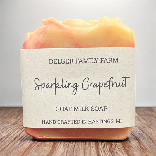 Bar of soap with a label reading 'Delger Family Farm Sparkling Grapefruit Goat Milk Soap' on a wooden surface.