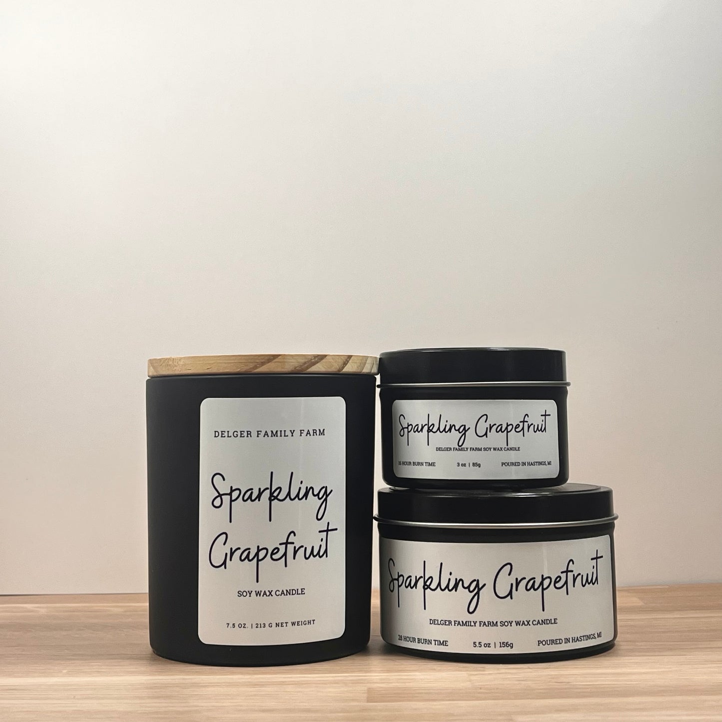 Three 'Sparkling Grapefruit' candles stacked on a wooden surface with a neutral background