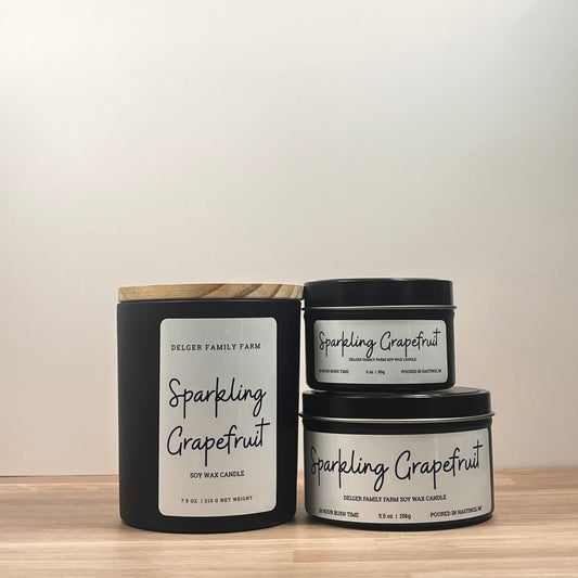 Three 'Sparkling Grapefruit' candles stacked on a wooden surface with a neutral background