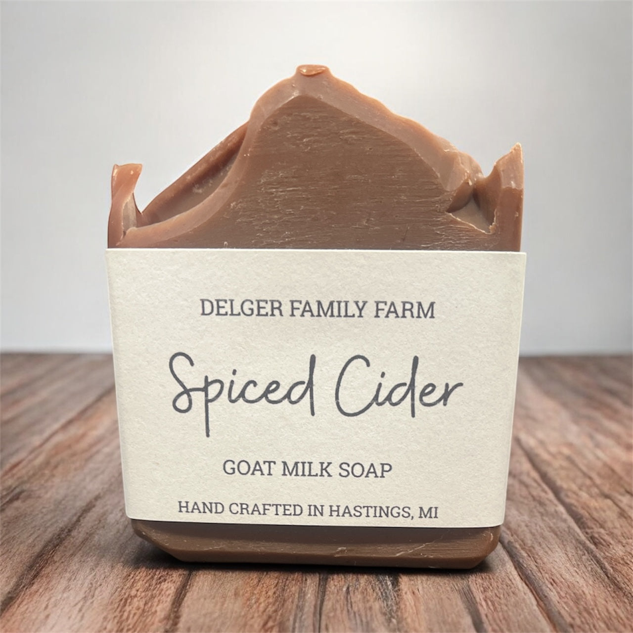 Bar of goat milk soap labeled 'Spiced Cider' from Delger Family Farm on a wooden surface.