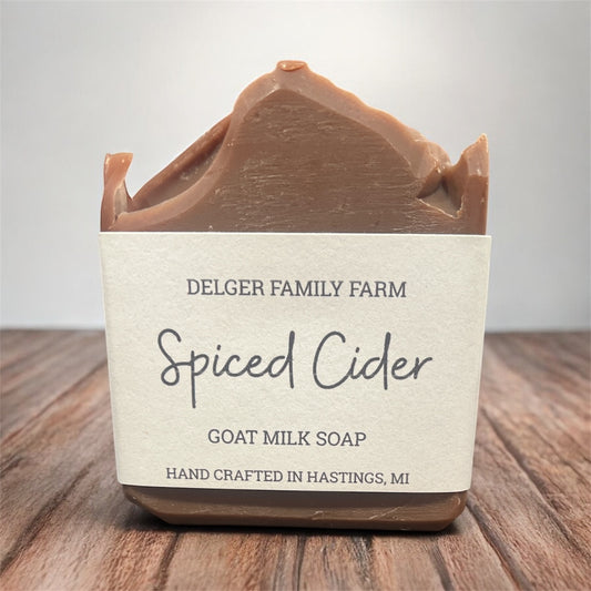 Bar of goat milk soap labeled 'Spiced Cider' from Delger Family Farm on a wooden surface.