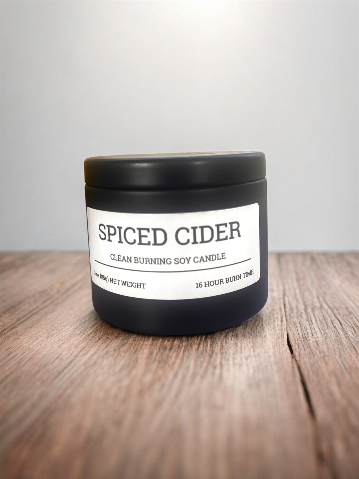 Spiced Cider candle in a black container on a wooden surface with a white background