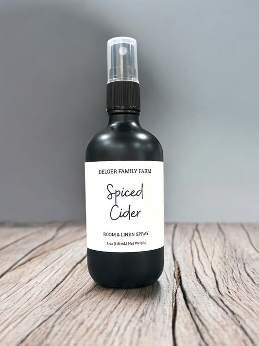 Black spray bottle labeled 'Spiced Cider' by Delger Family Farm on a wooden surface with a gray background.