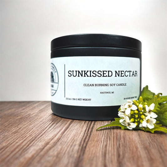 Candle labeled 'Sunkissed Nectar' on a wooden surface with flowers.