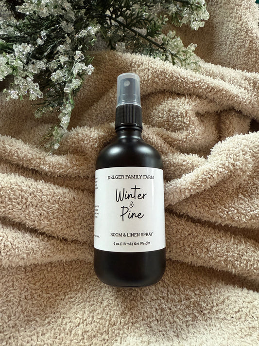 Room spray bottle labeled 'Winter & Pine' by Delger Family Farm on a textured surface with decorative elements.