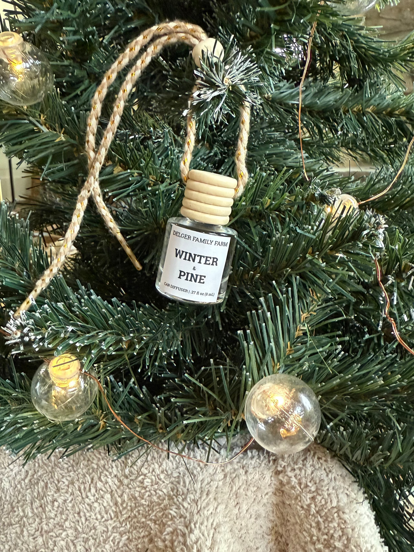 Small bottle labeled 'Winter Pine' hanging on a decorated Christmas tree.
