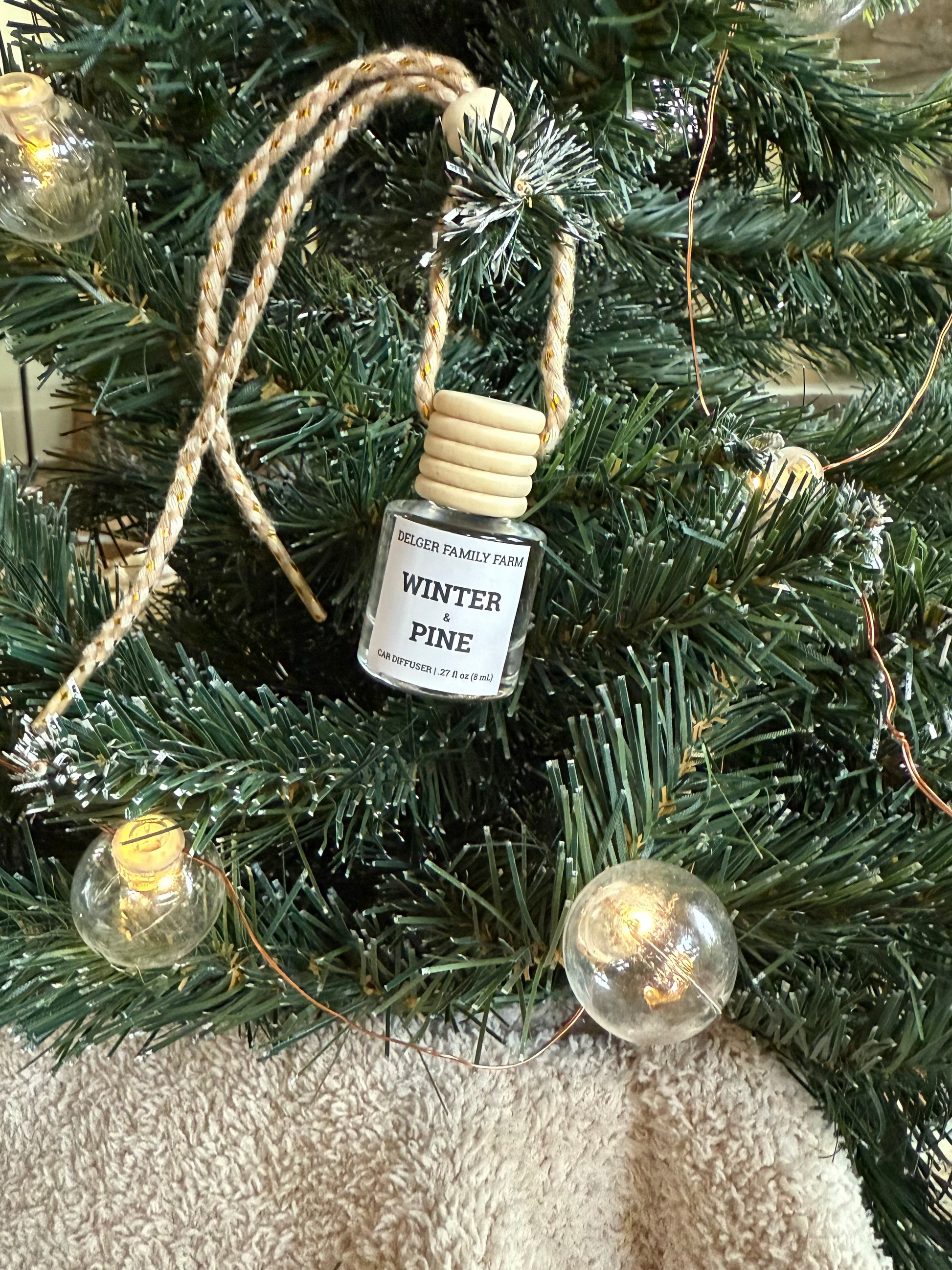Small bottle labeled 'Winter Pine' hanging on a decorated Christmas tree.