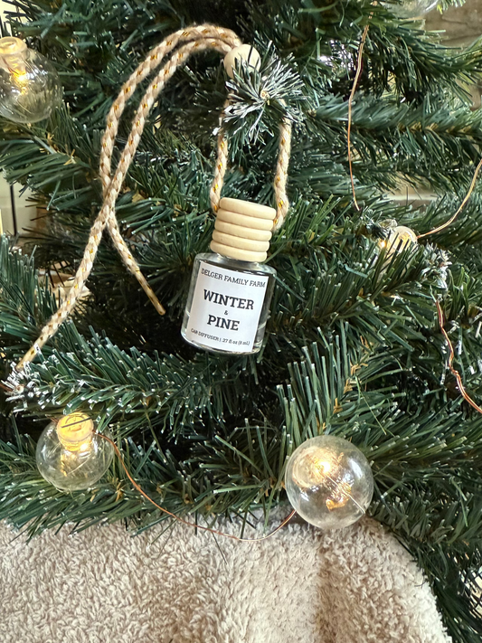 Small bottle labeled 'Winter Pine' hanging on a decorated Christmas tree.